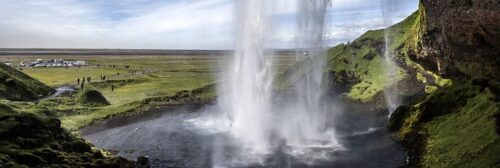 IJslandse waterval met toeristen en weelderig groen landschap.