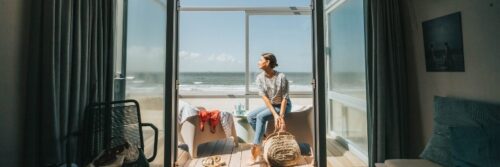 Vrouw geniet van uitzicht op zee vanuit strandhotelkamer.